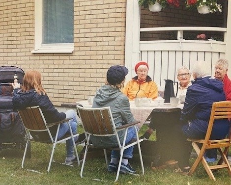 Ett glatt gäng äldre personer runt ett bord med kaffetermos och koppar