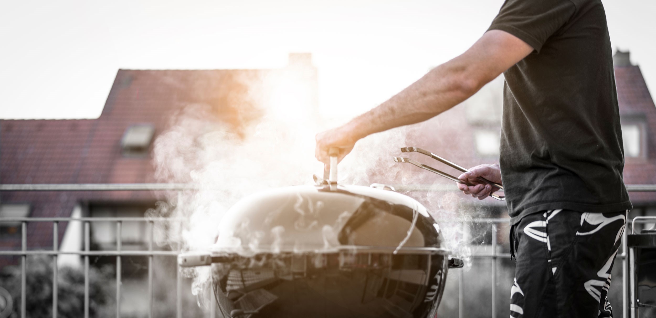 En person i mörka kläder som står bredvid en grill som det ryker ur